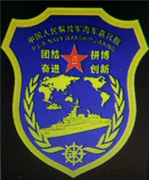 053H3型護(hù)衛(wèi)艦嘉興艦的艦徽，正上方艦訓(xùn)環(huán)繞八一軍徽，下方為世界地圖和艦艇示意圖，兩側(cè)為象征和平的橄欖枝，整個設(shè)計中規(guī)中矩。